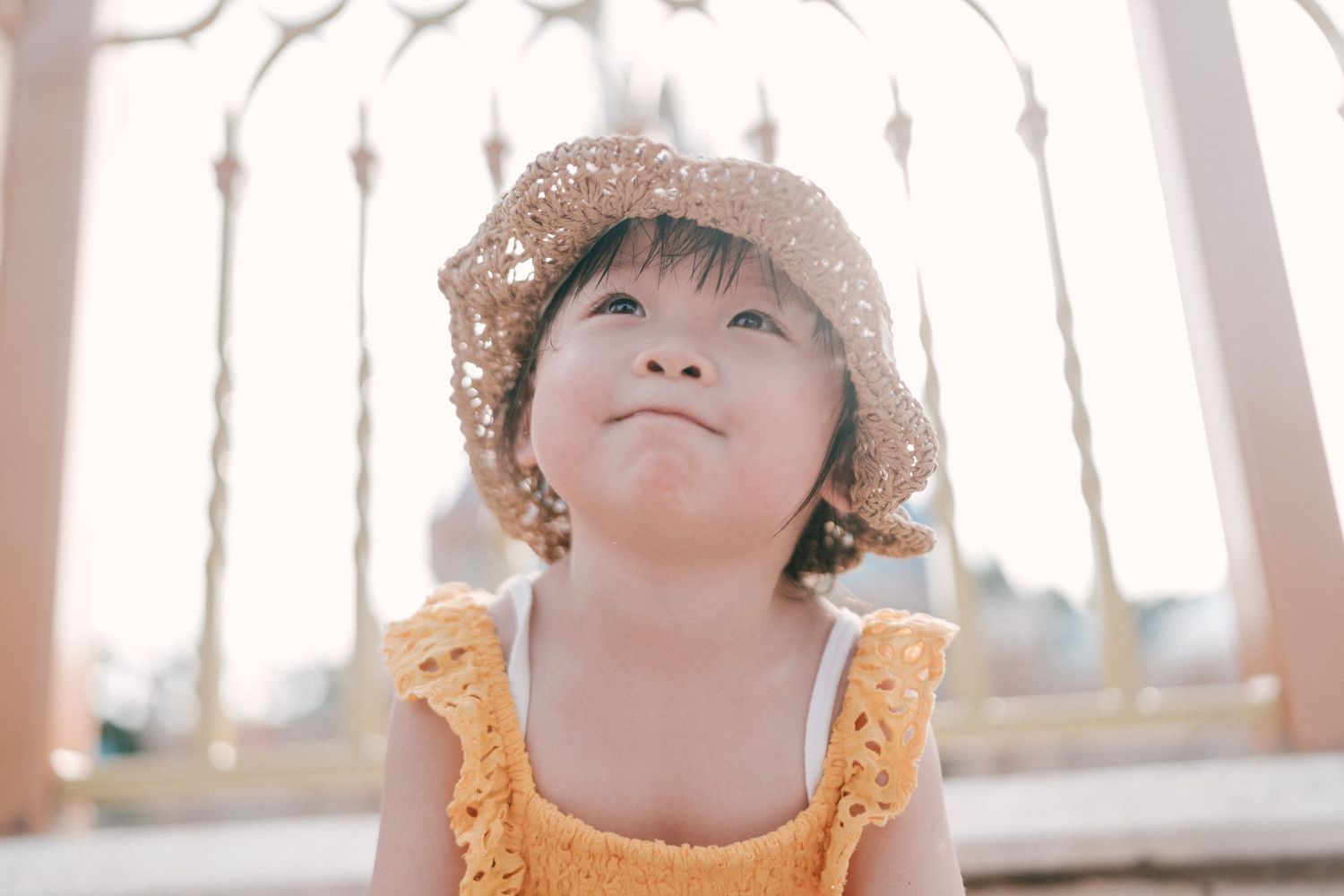 Child in yellow dress and straw hat looks up with wonder.