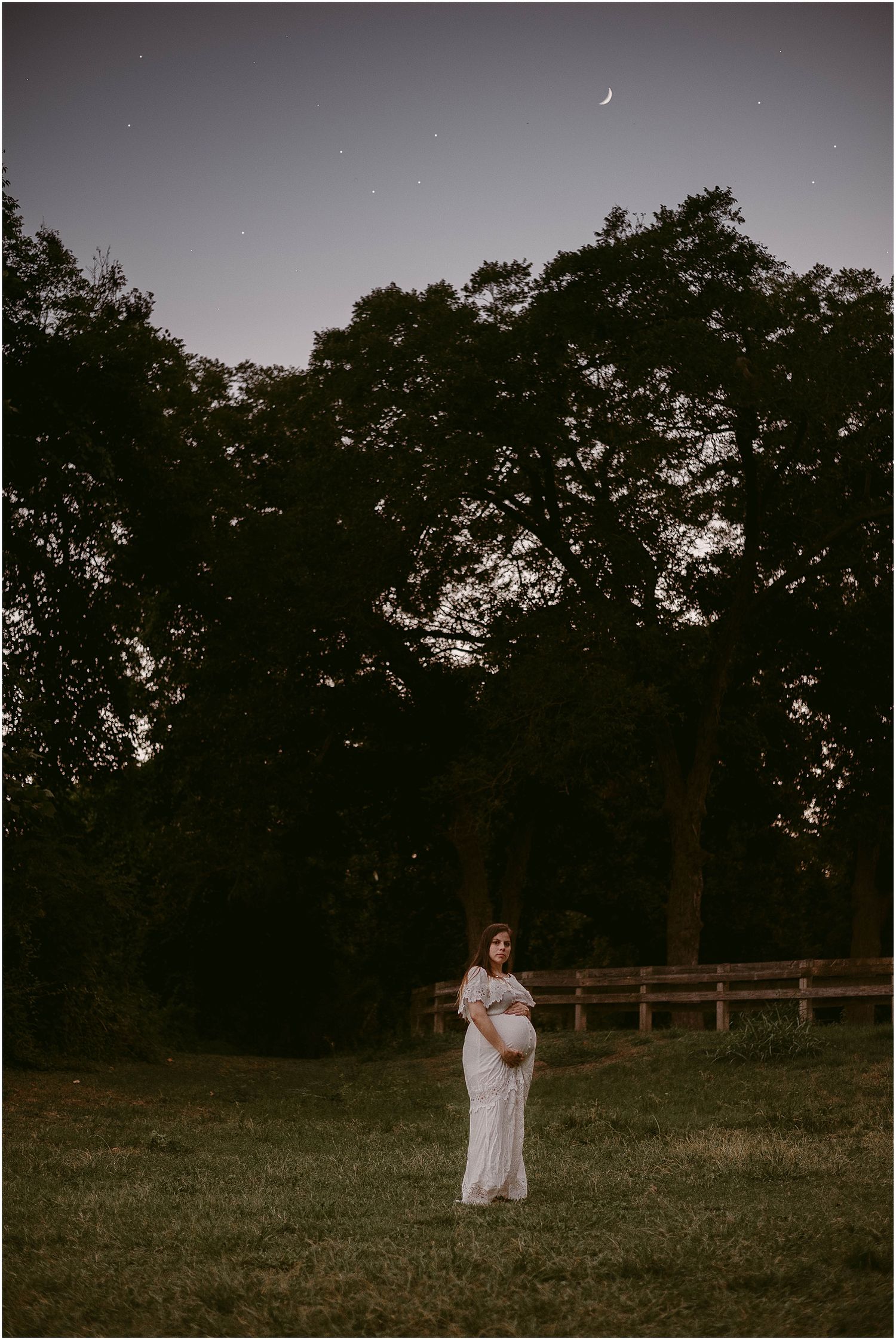 Ethereal nighttime maternity photo with crescent moon and silhouetted trees.