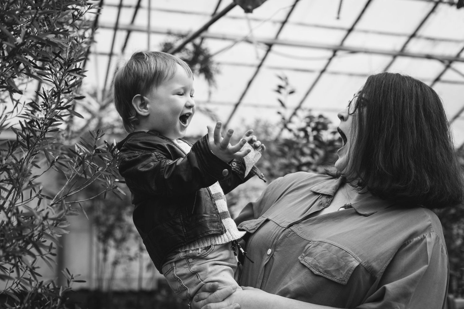 A joyful interaction between parent and child in a sunlit greenhouse setting.