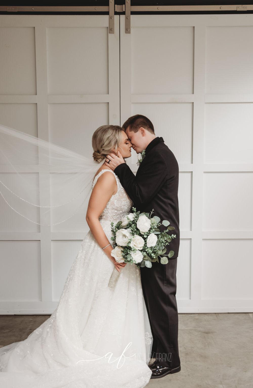 Romantic wedding couple embracing against modern white paneled wall.