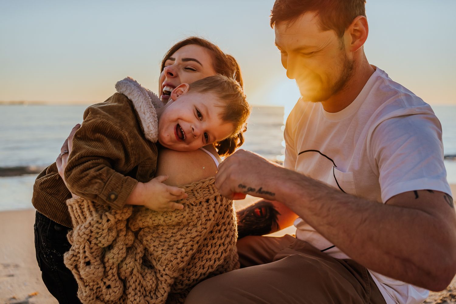 A father and son fist bumping while hugging mum on the beach at sunset