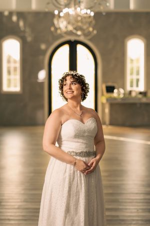 Bride strikes a regal pose on the venue dance floor as natural sunlight pours in through the door and windows behind her