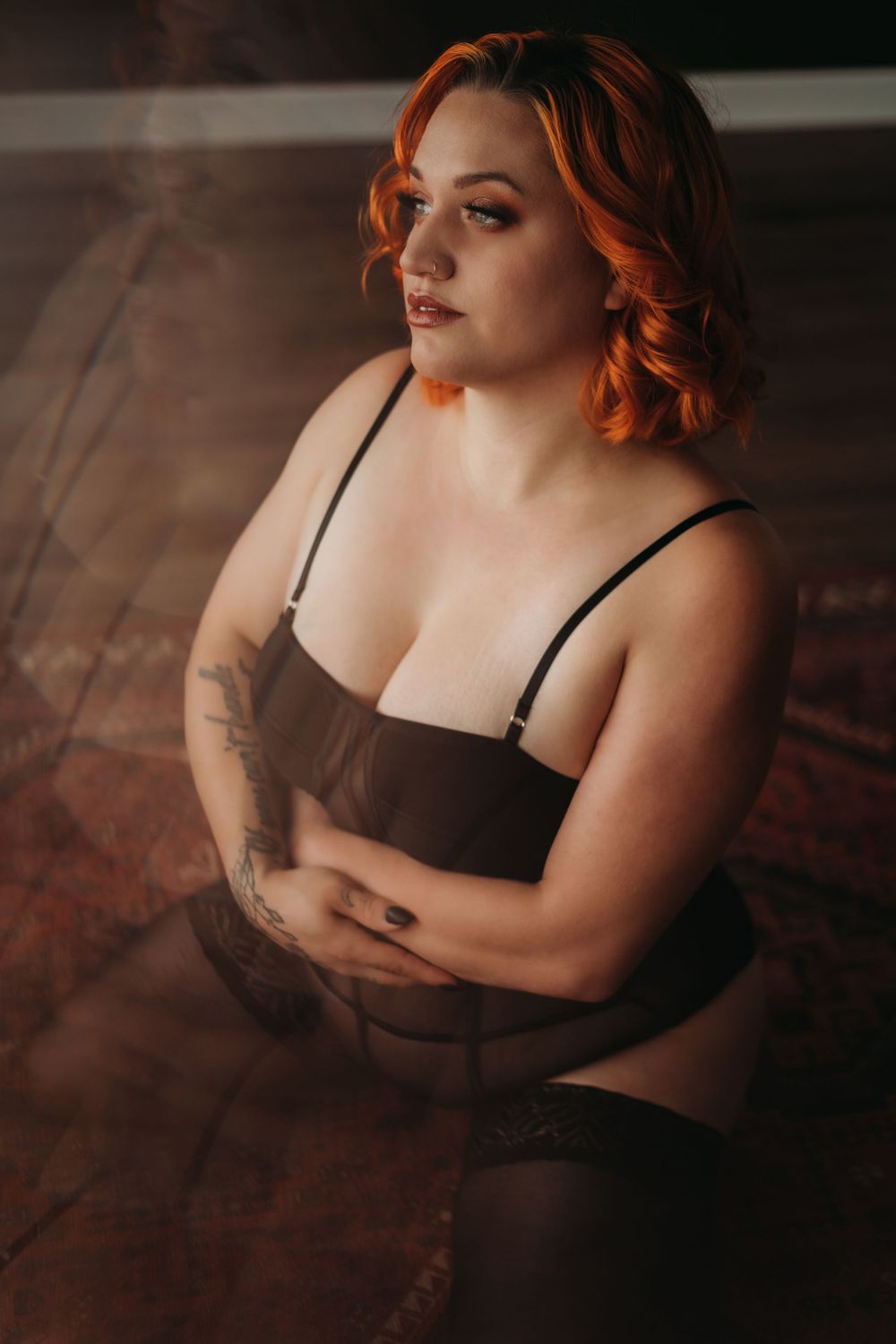 Intimate boudoir portrait featuring warm lighting on person in black lingerie against wooden floor.
