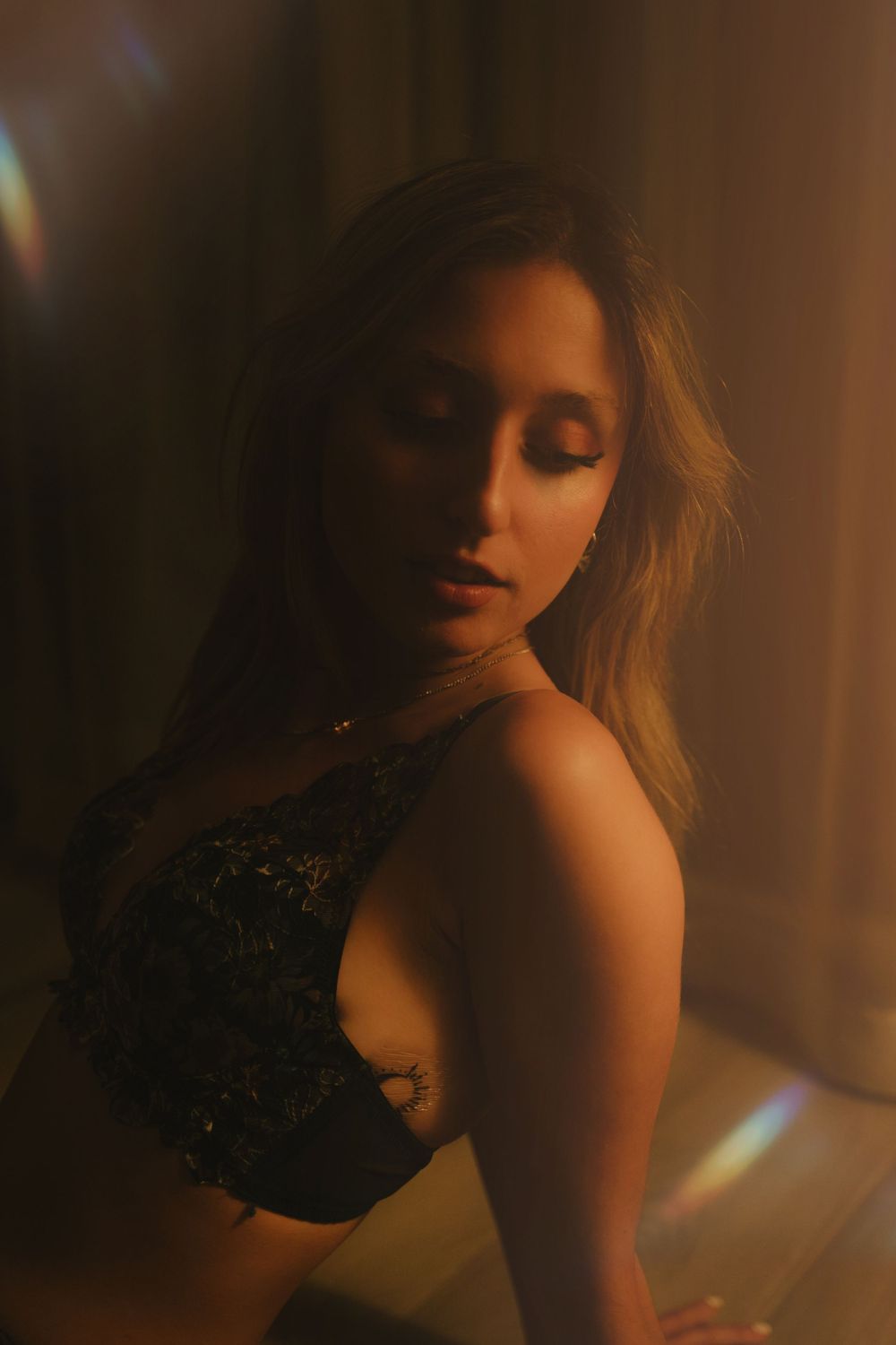 Atmospheric boudoir portrait with warm moody lighting and black lace details.