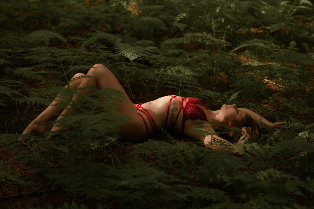 Person in red swimwear lying among ferns in mystical forest setting.