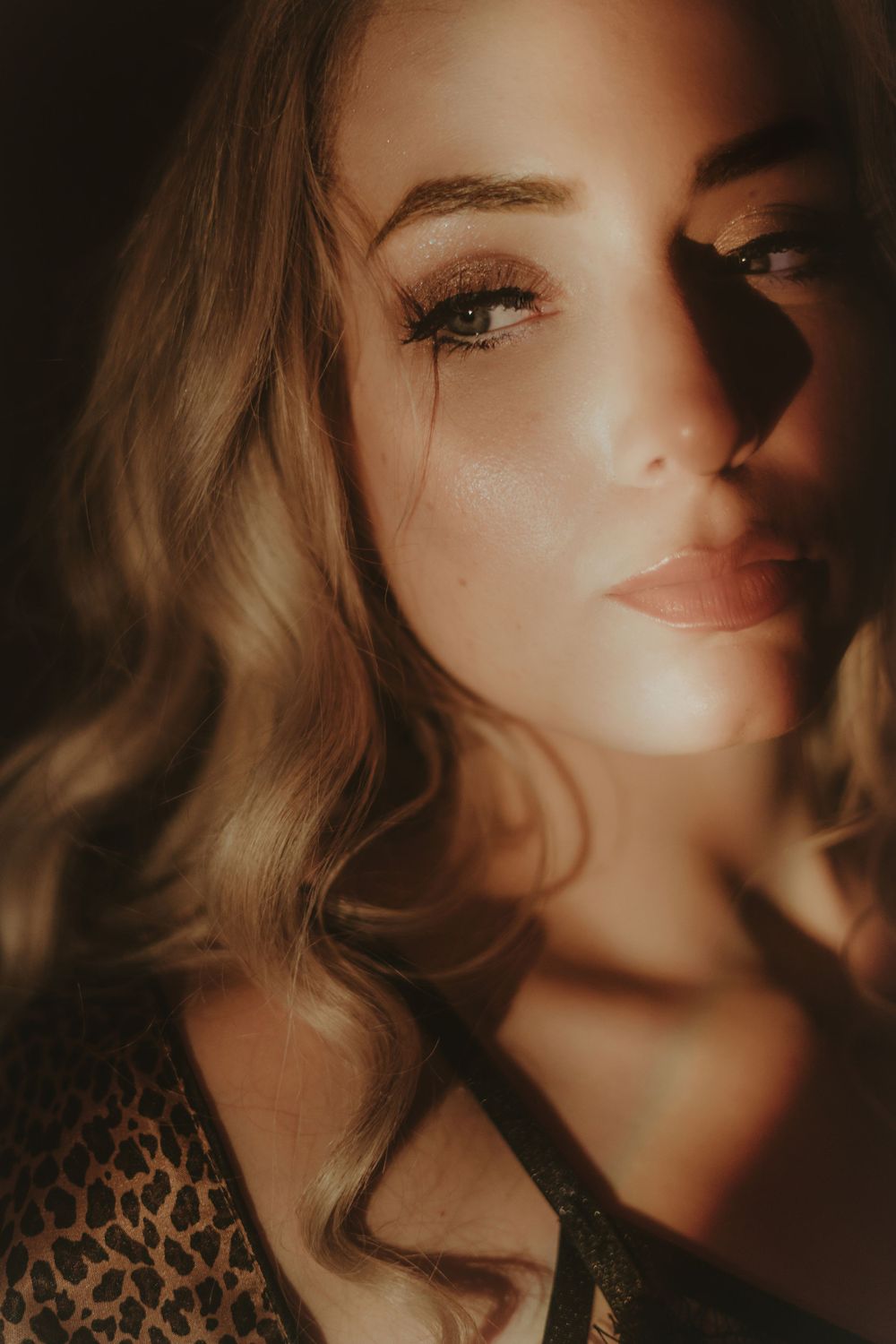 Dramatic close-up portrait with glamorous makeup in warm lighting.