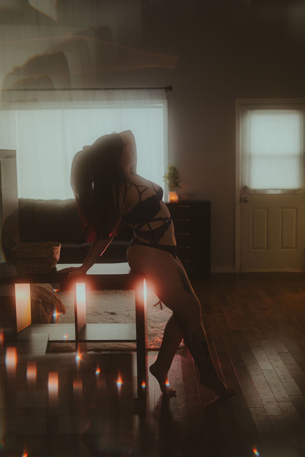 Silhouetted figure on chair surrounded by candlelight in moody room setting.