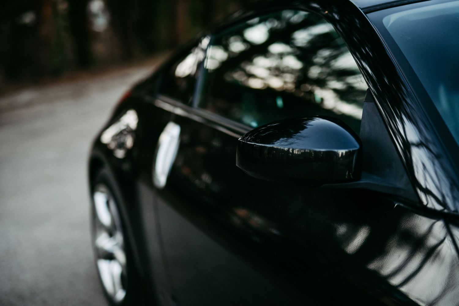 Side mirror detail of black Nissan sports car with trees reflecting.