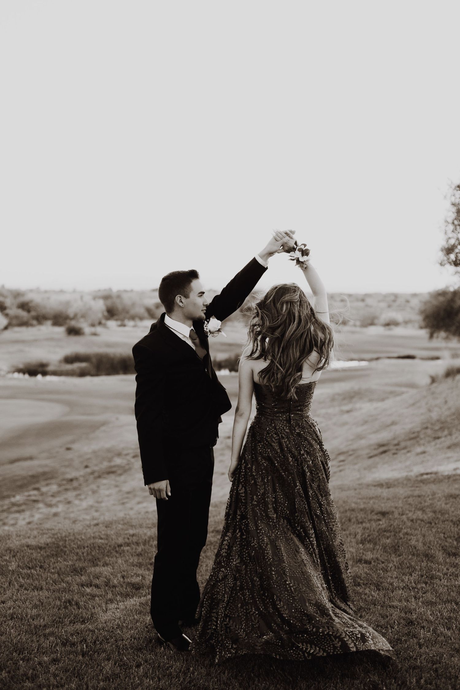 Black and white photo of a dancing couple in formal wear on a grassy field.