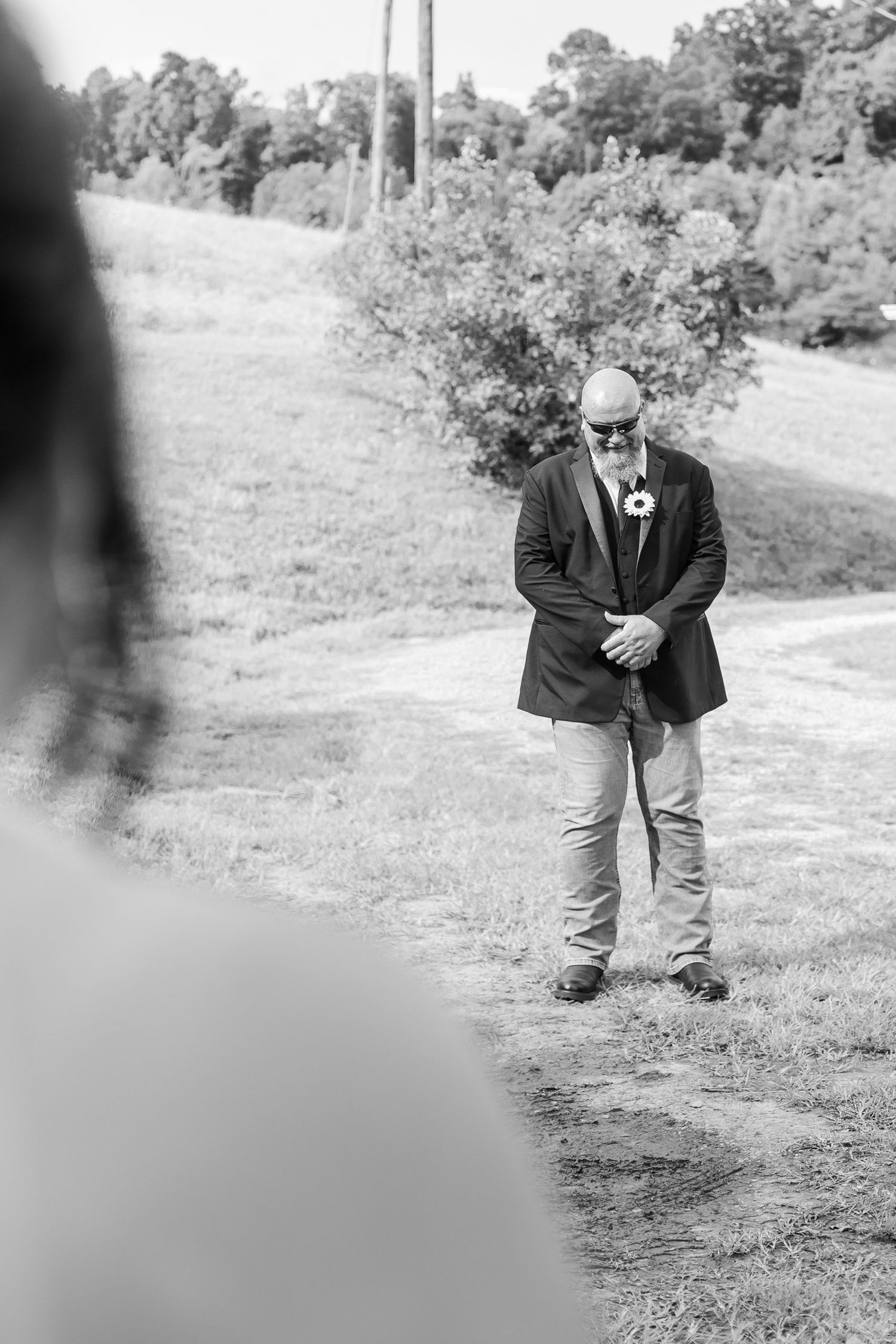 Person in a black suit jacket and jeans stands on a dirt path during an outdoor photoshoot.