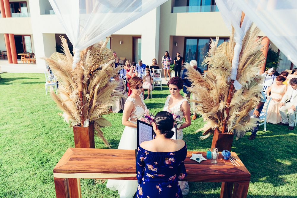 A beach wedding ceremony setup with pampas grass decorations and guests seated on wooden benches.