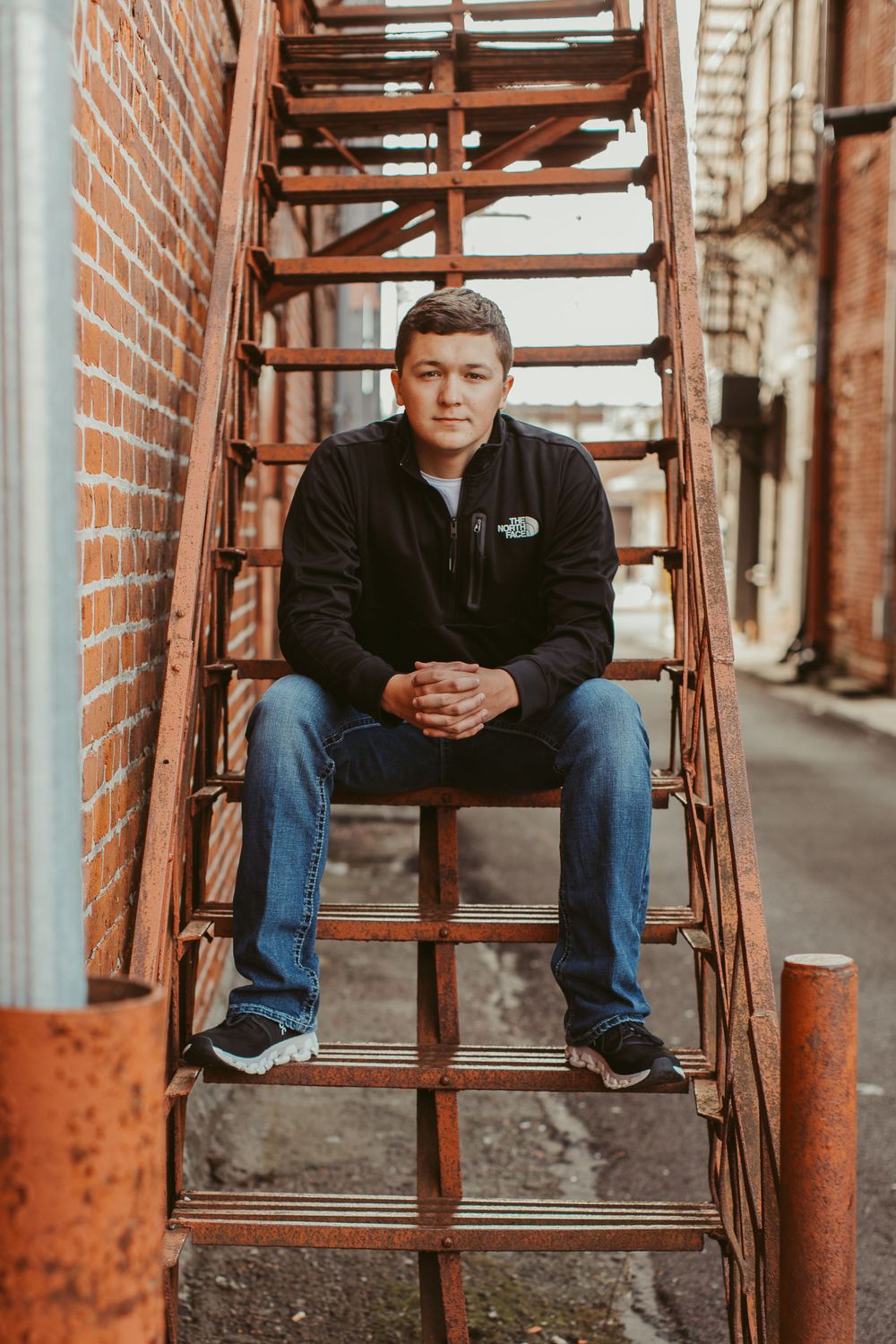 Person sitting on rustic metal fire escape stairs against brick building backdrop.