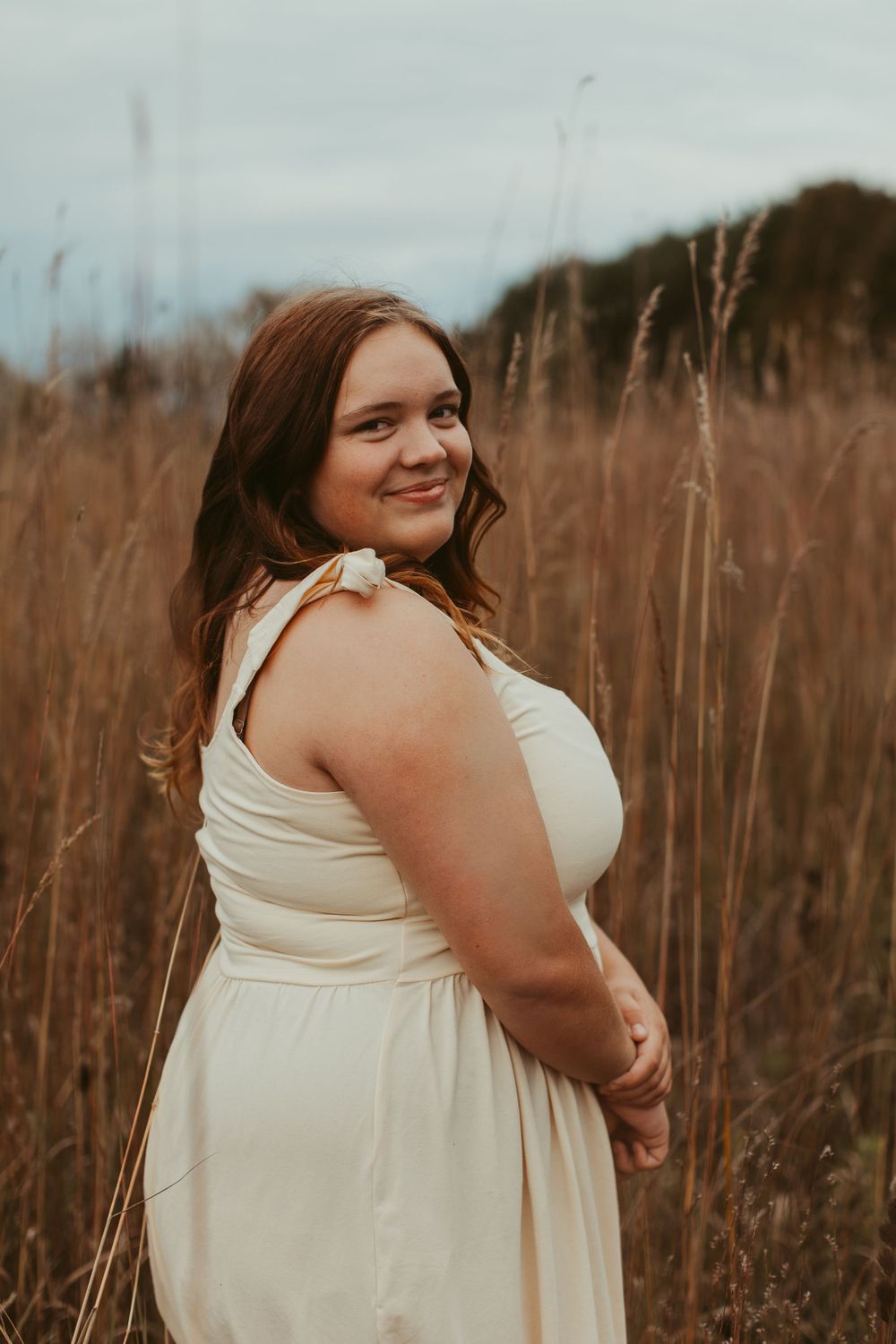Person in cream dress standing in field of tall grass during golden hour.