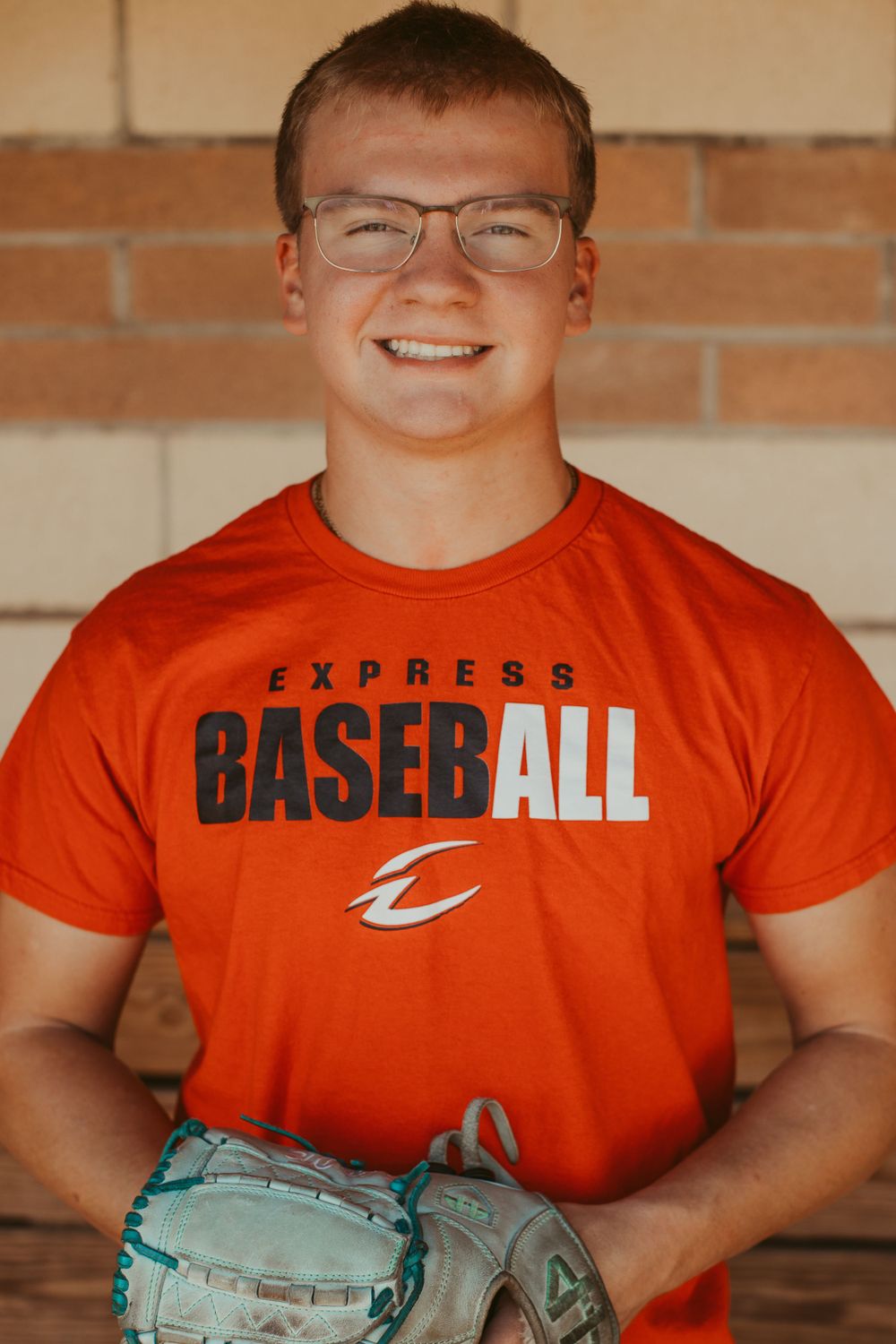 Baseball player wearing bright orange t-shirt holding baseball glove.