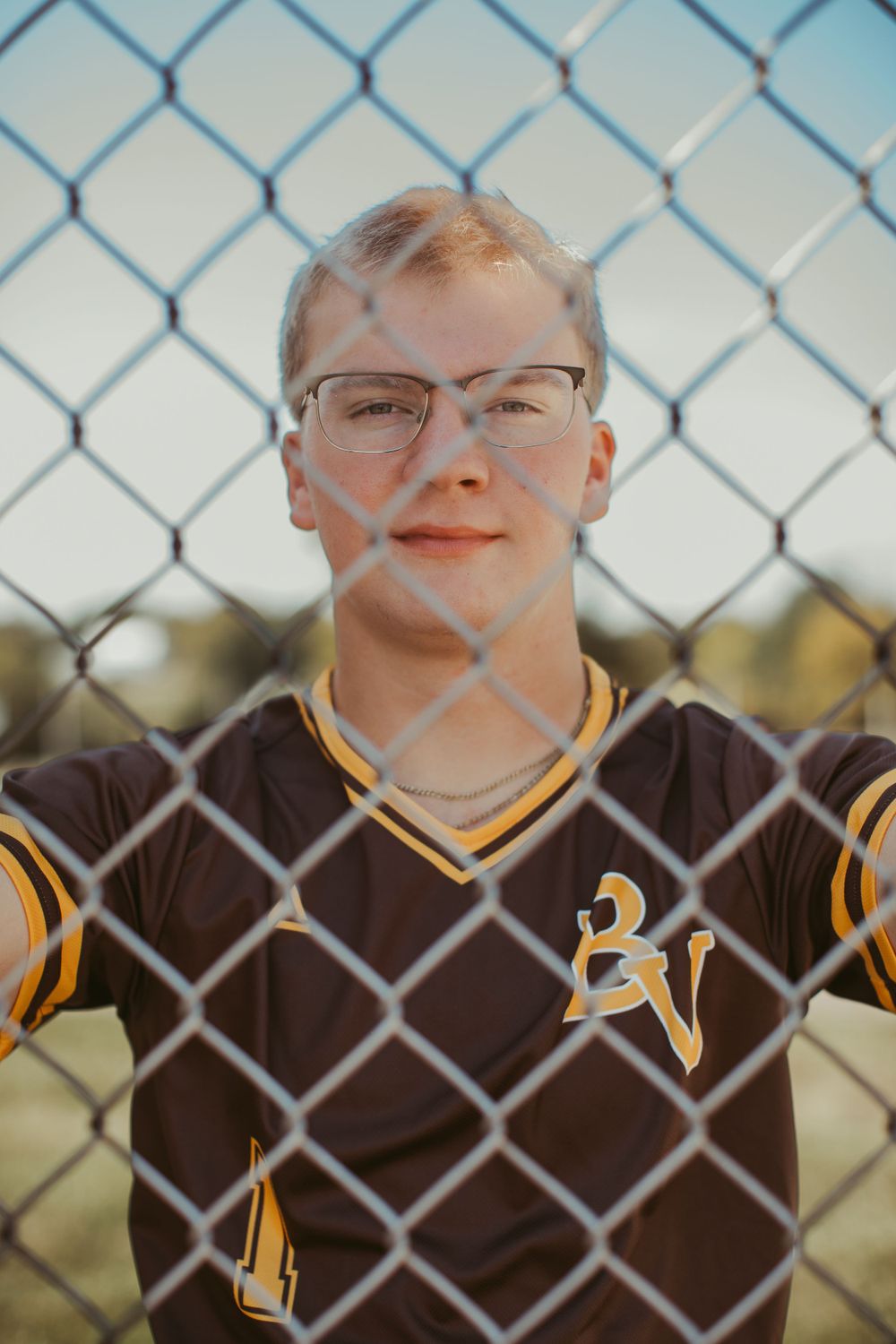 Portrait through chain link fence wearing black and yellow sports uniform.