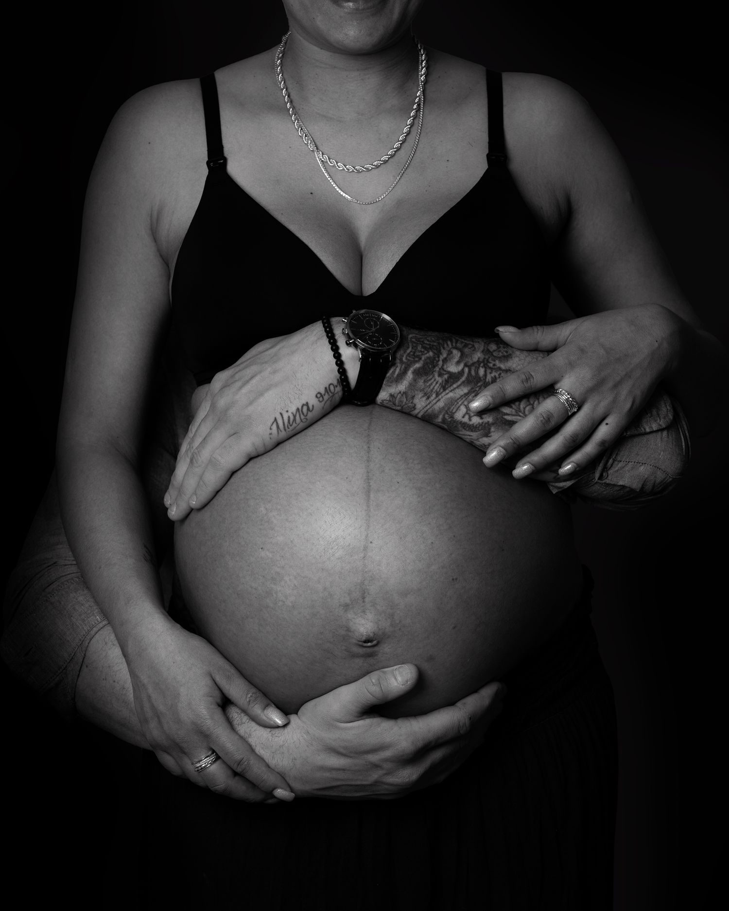 Svart vit bild av gravid mage där mamman och partnern håller om magen