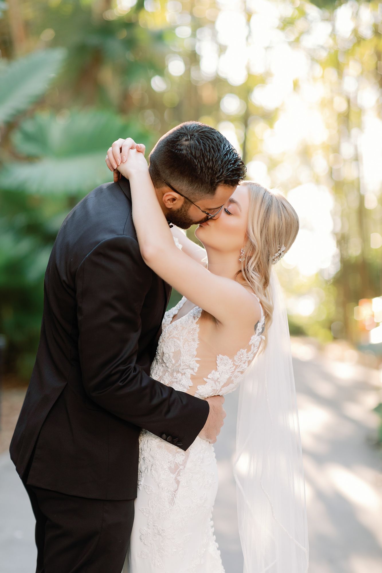 A romantic wedding couple shares an intimate kiss outdoors in soft golden sunlight.