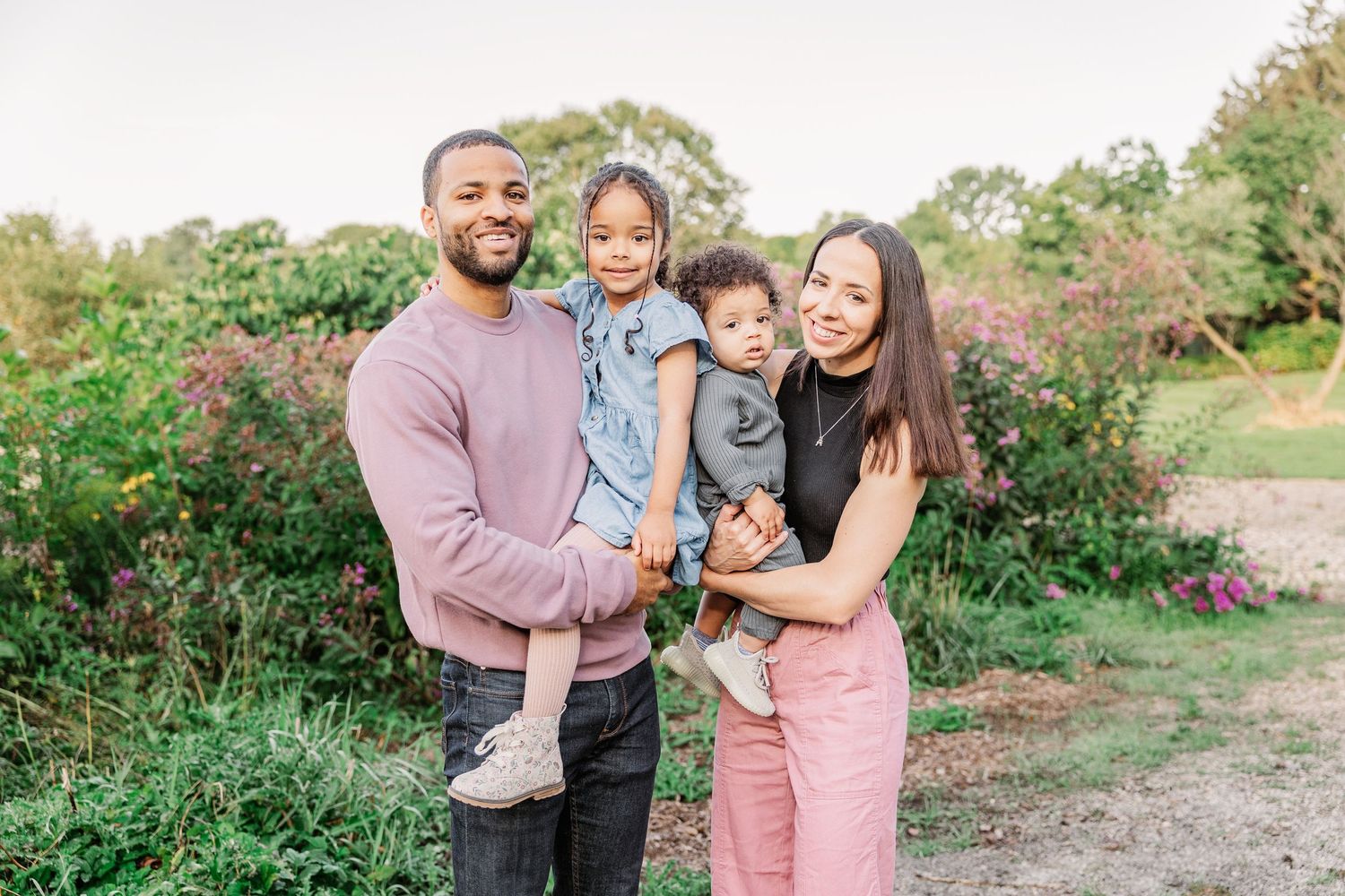 Family of four poses together outdoors among blooming pink flowers.