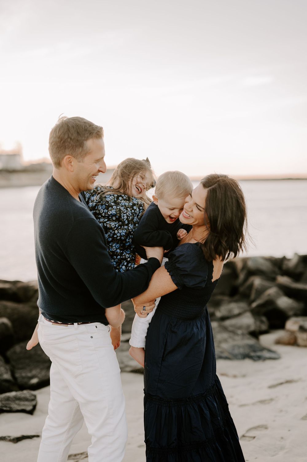 Family playing and laughing together on sandy beach at dusk.