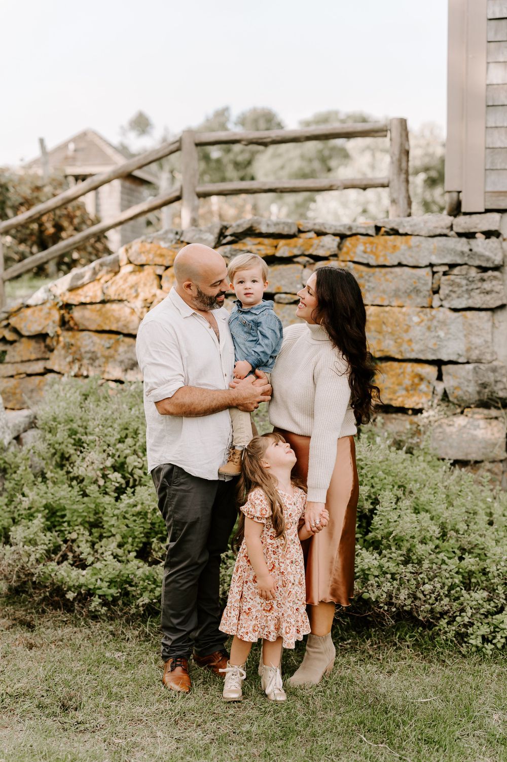Family posing together by rustic stone wall in garden setting.