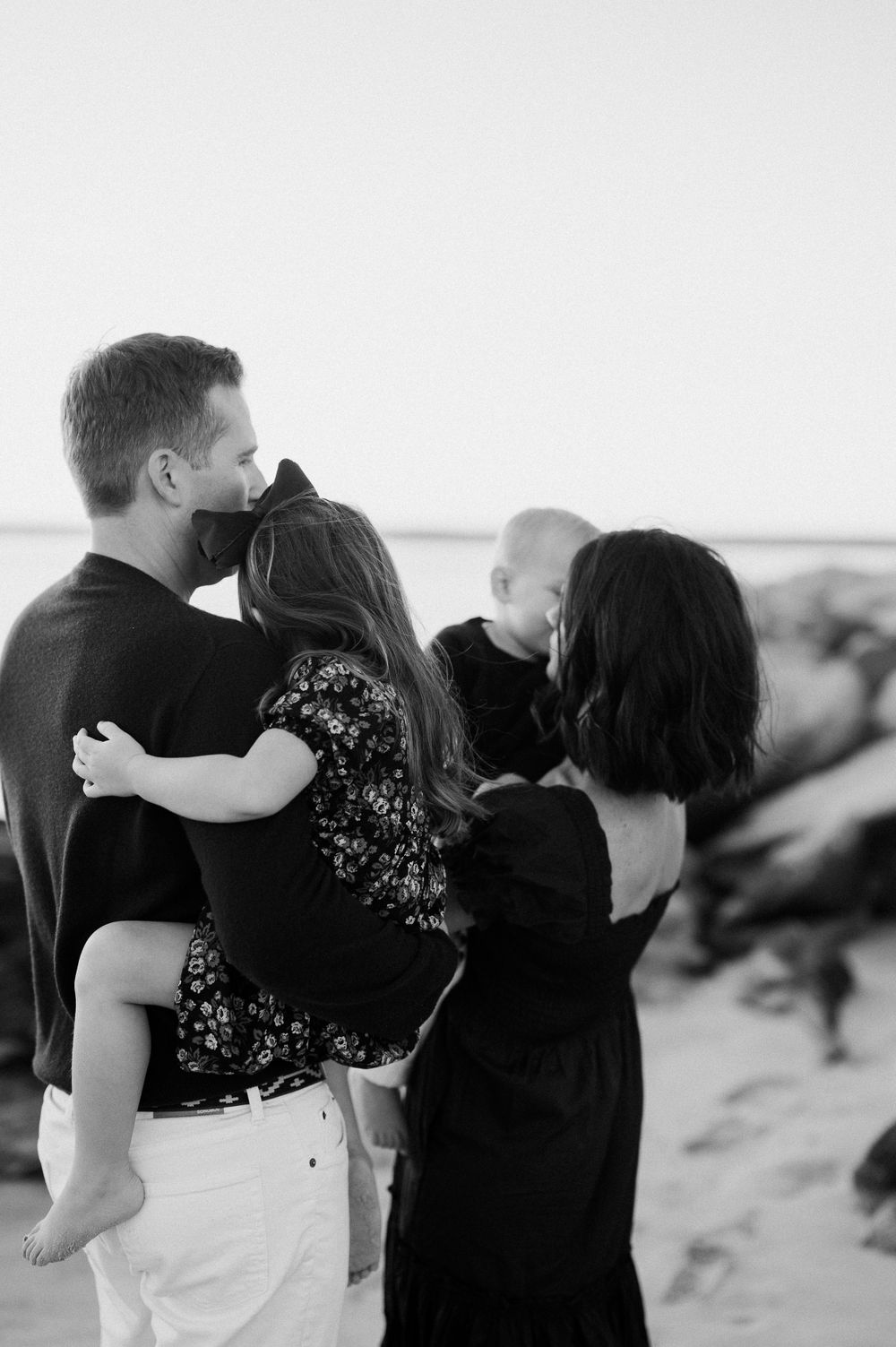 Family embracing on beach at sunset in black and white.