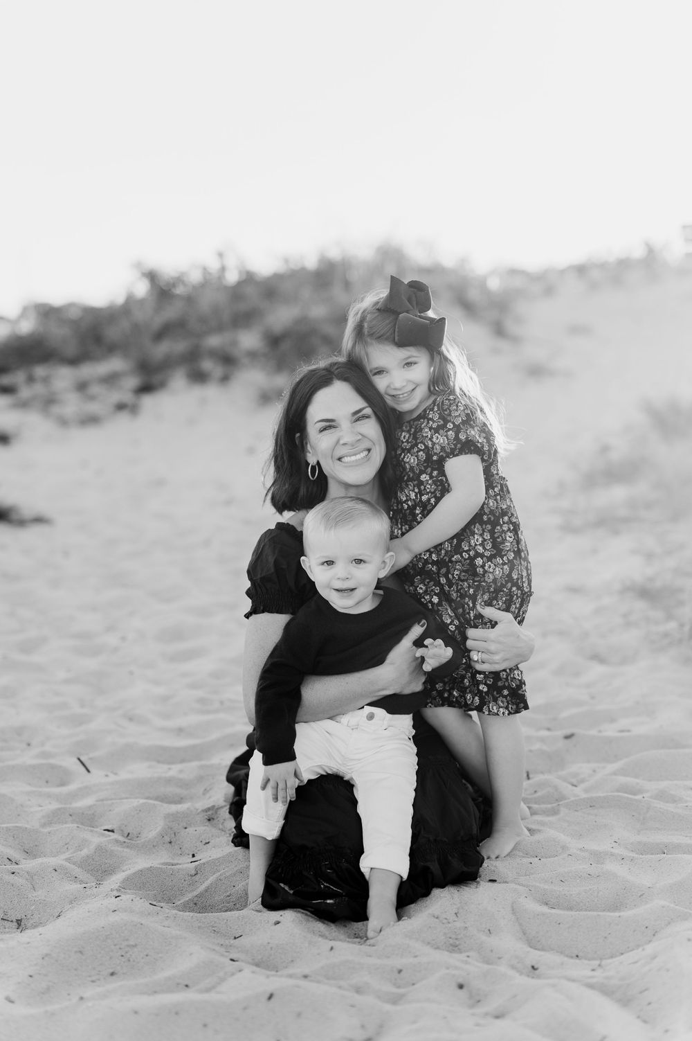 Family playing together on sandy beach in black and white photography.