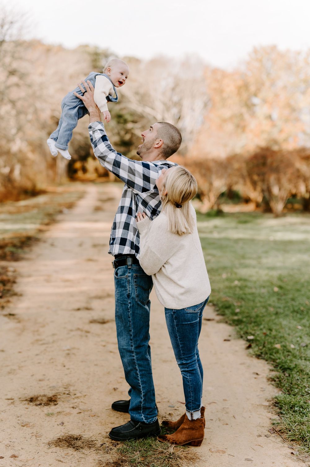 Family playing and lifting child together on a sunny autumn path.