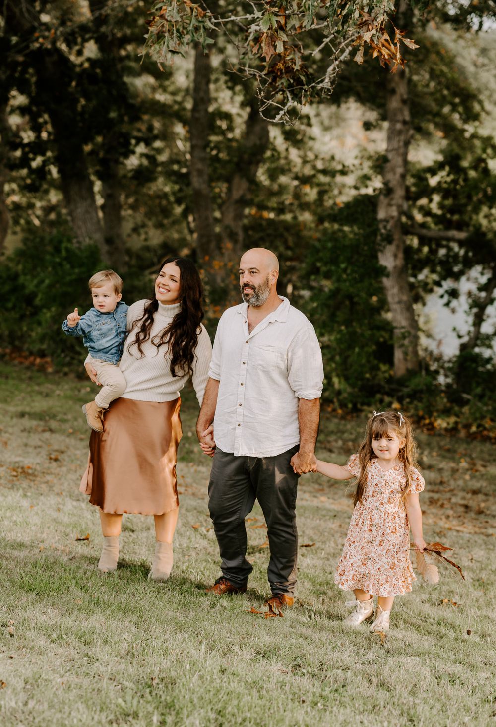 Family walking together on a grassy slope during golden hour in coordinated autumn outfits.