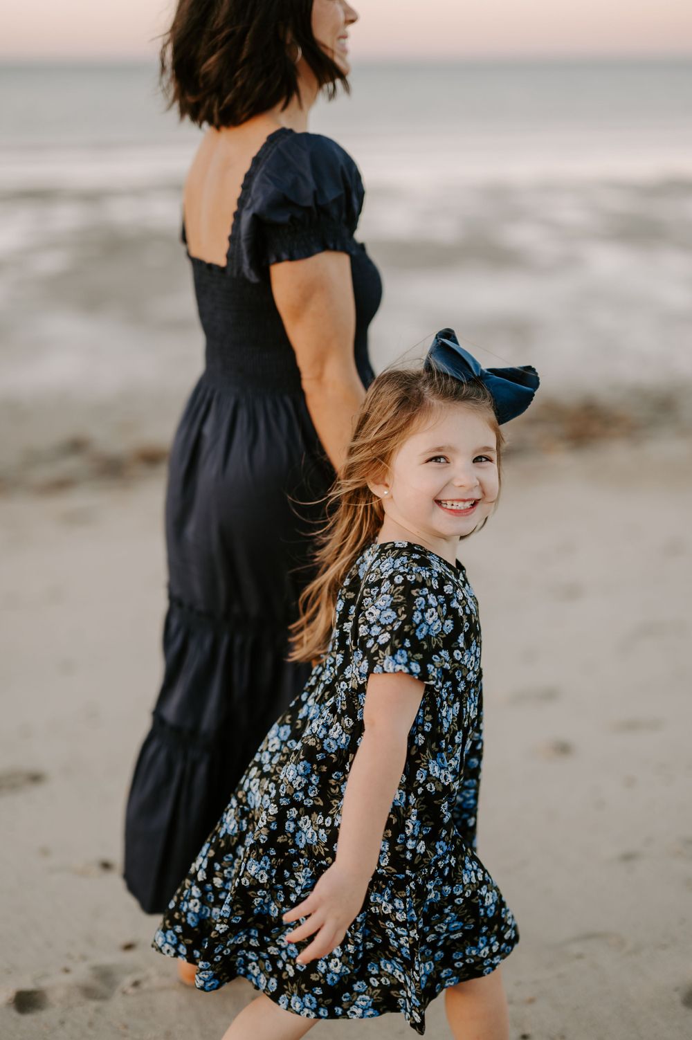 Family walking along beach at sunset in coordinated navy and floral outfits.
