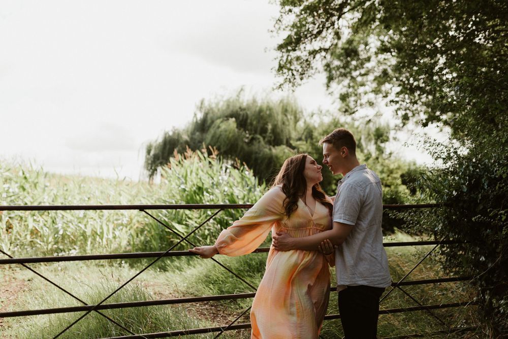 A couple embraces by a rustic fence overlooking a scenic natural landscape.