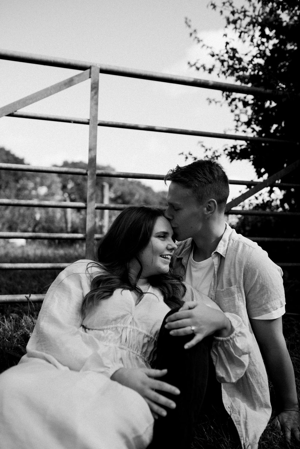 A romantic black and white moment captured between two people near a metal railing outdoors.