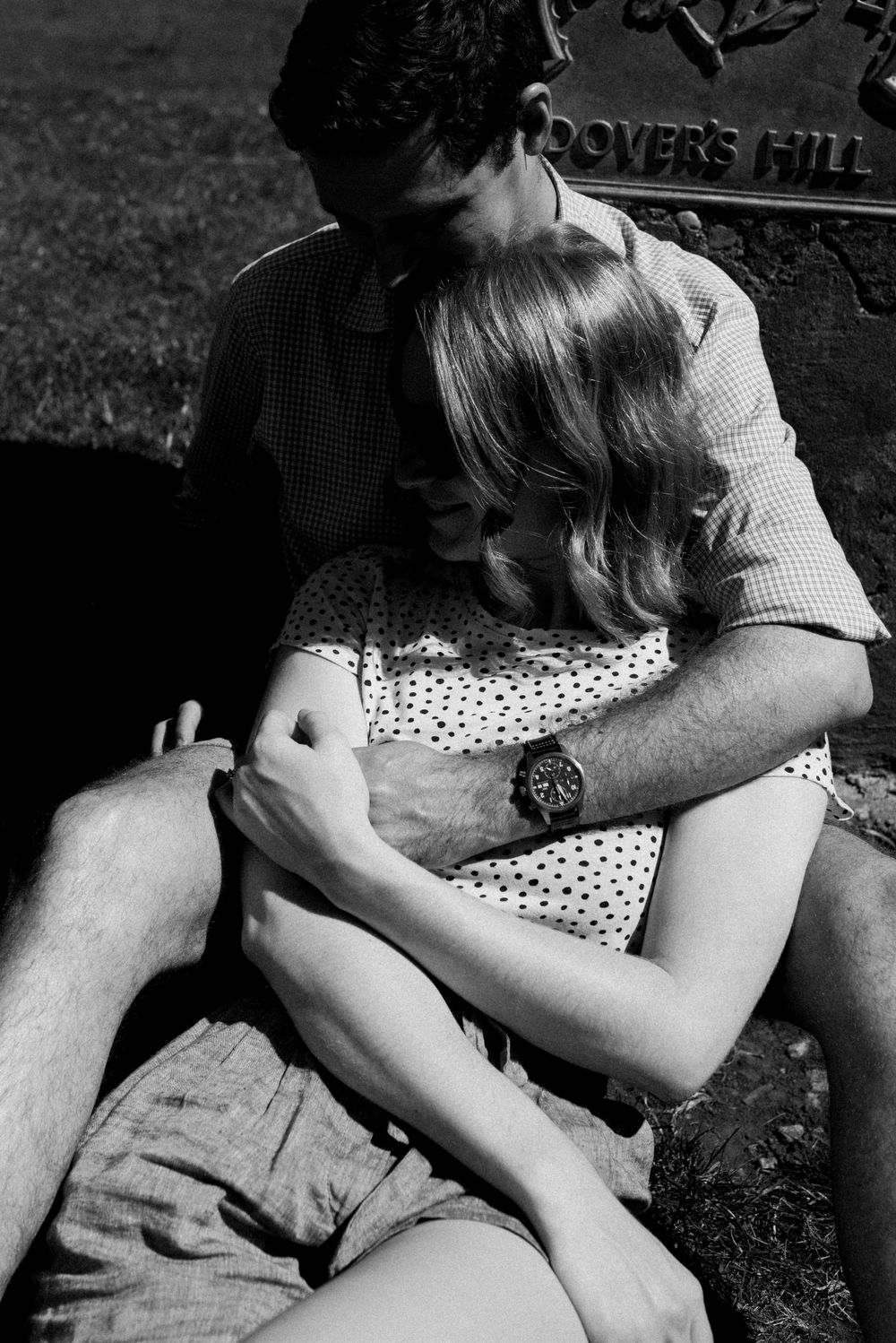 Black and white photo of couple sitting close together outdoors near stone marker.