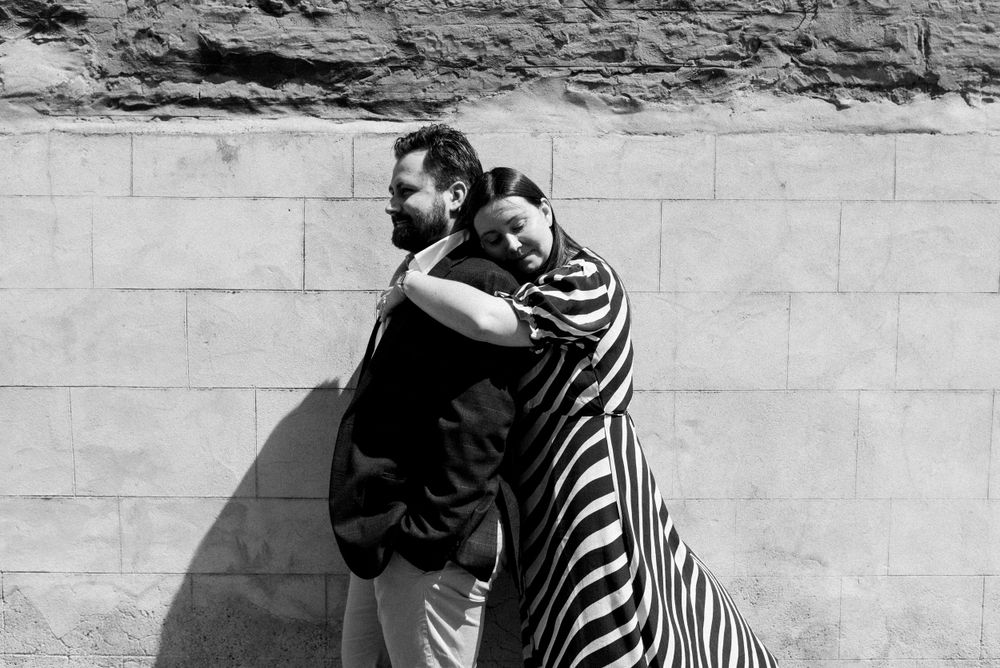 A dramatic black and white portrait of a couple embracing against a stone wall.
