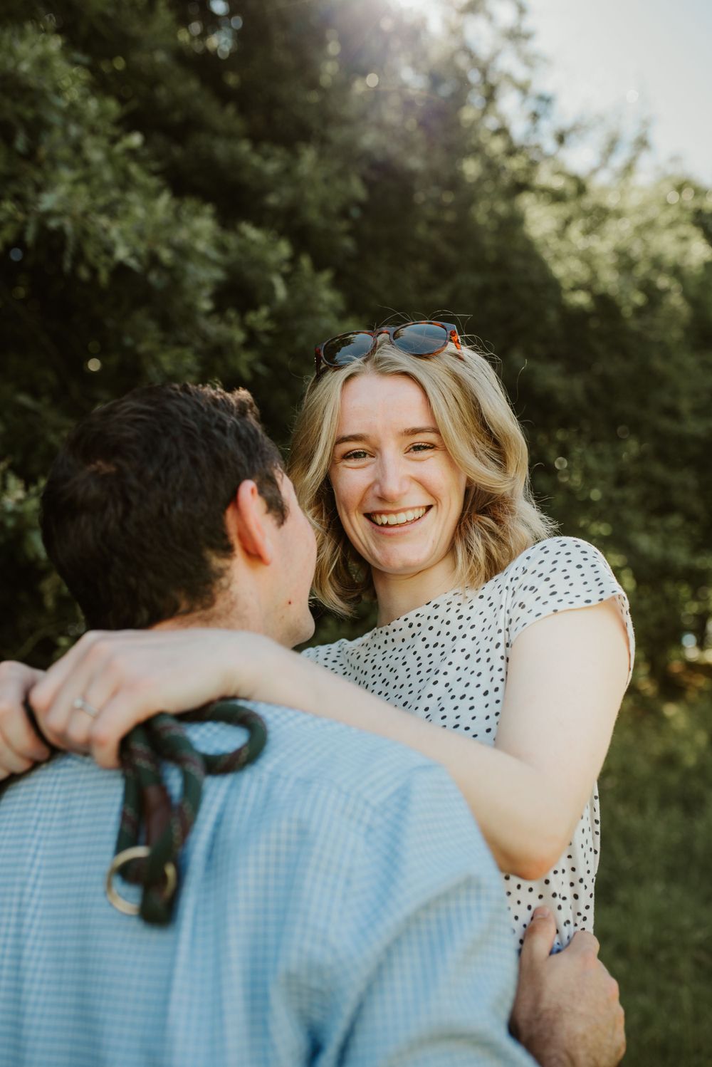 Intimate outdoor portrait of couple laughing together in sunlit garden setting.