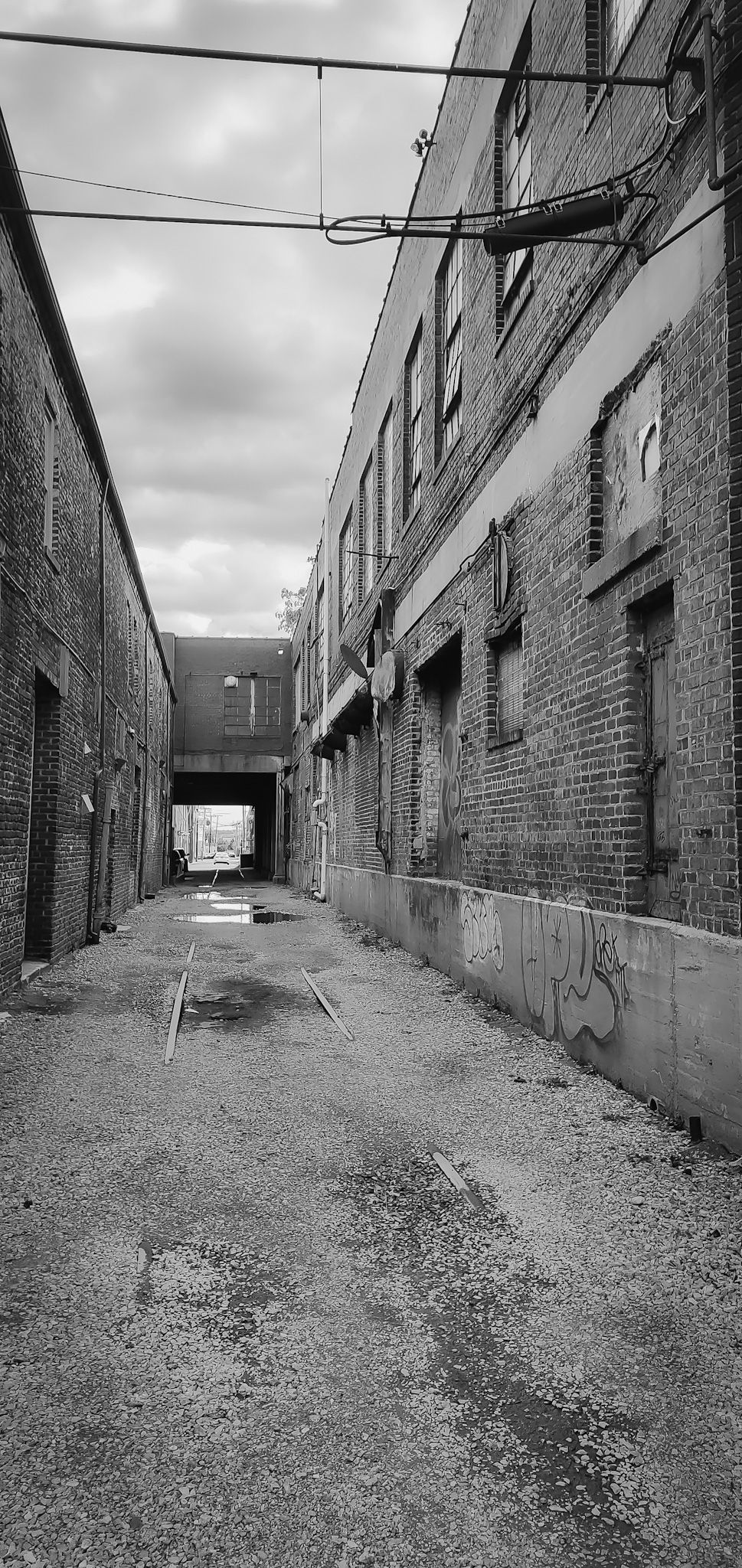 Moody black and white urban alley with brick walls and overhead wires leading to tunnel.