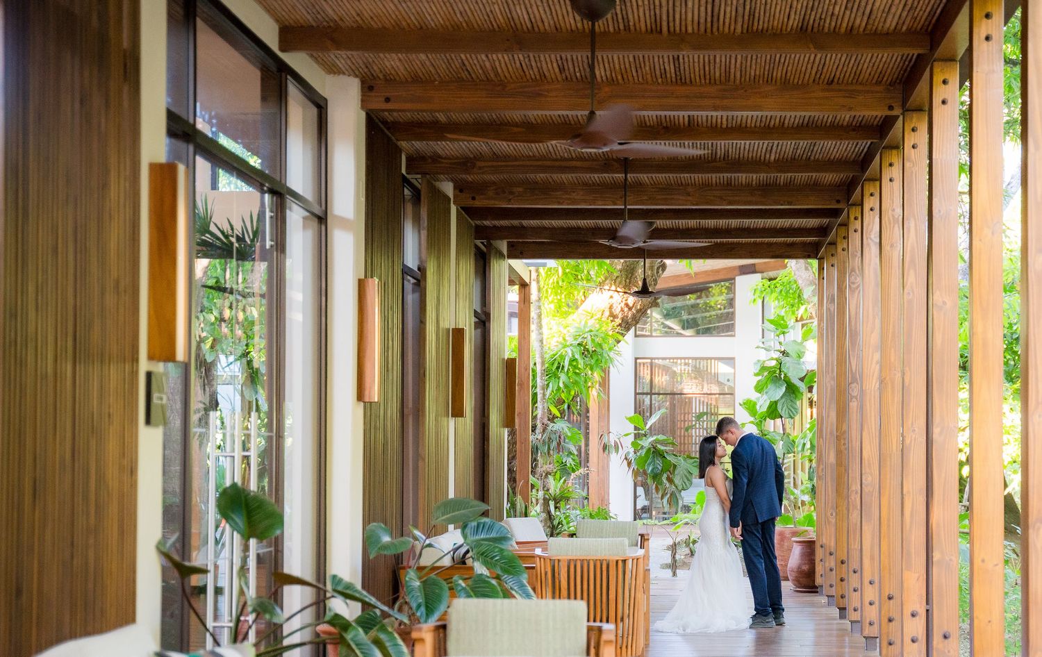 Couple walking down an outdoor rustic corridor with wooden beams and potted plants in Costa Rica, Botanika resort Osa Peninsula