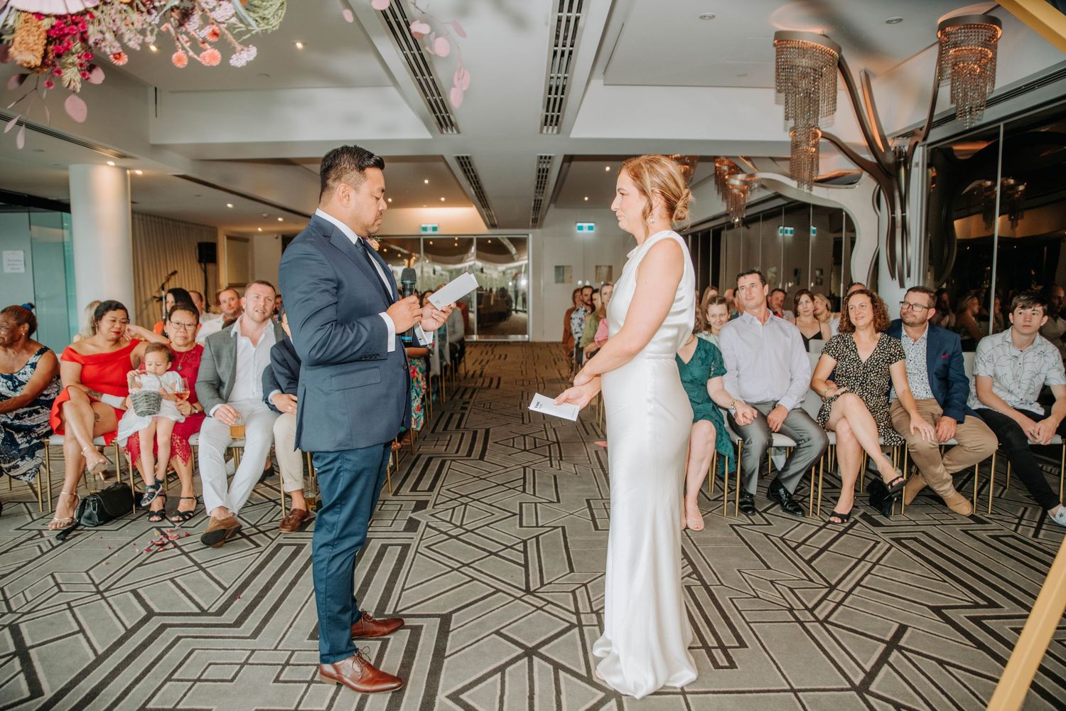 A couple exchanges vows during their indoor wedding ceremony surrounded by guests.