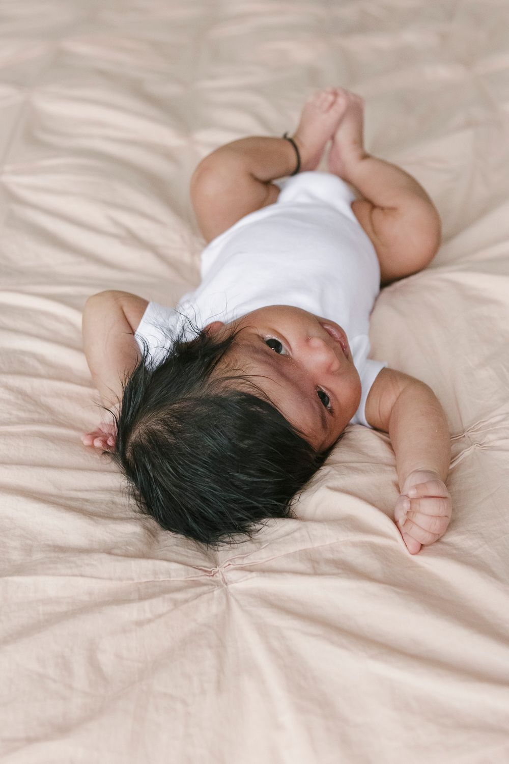 Adorable baby girl resting in bed during a newborn photo session at home in the Upper West Side, captured by NYC