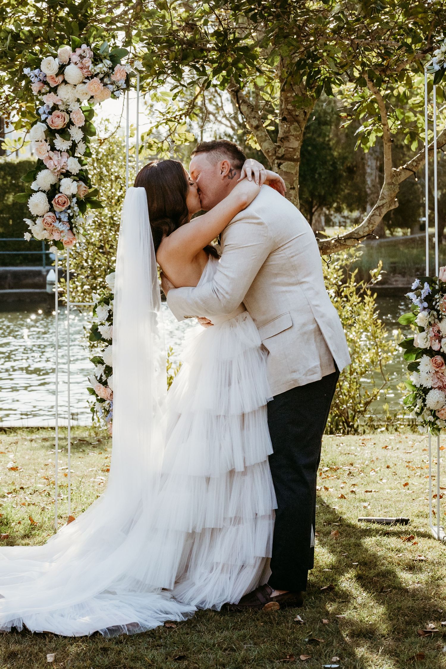 Newlyweds share their first kiss under a beautiful floral arch in an outdoor garden wedding ceremony.