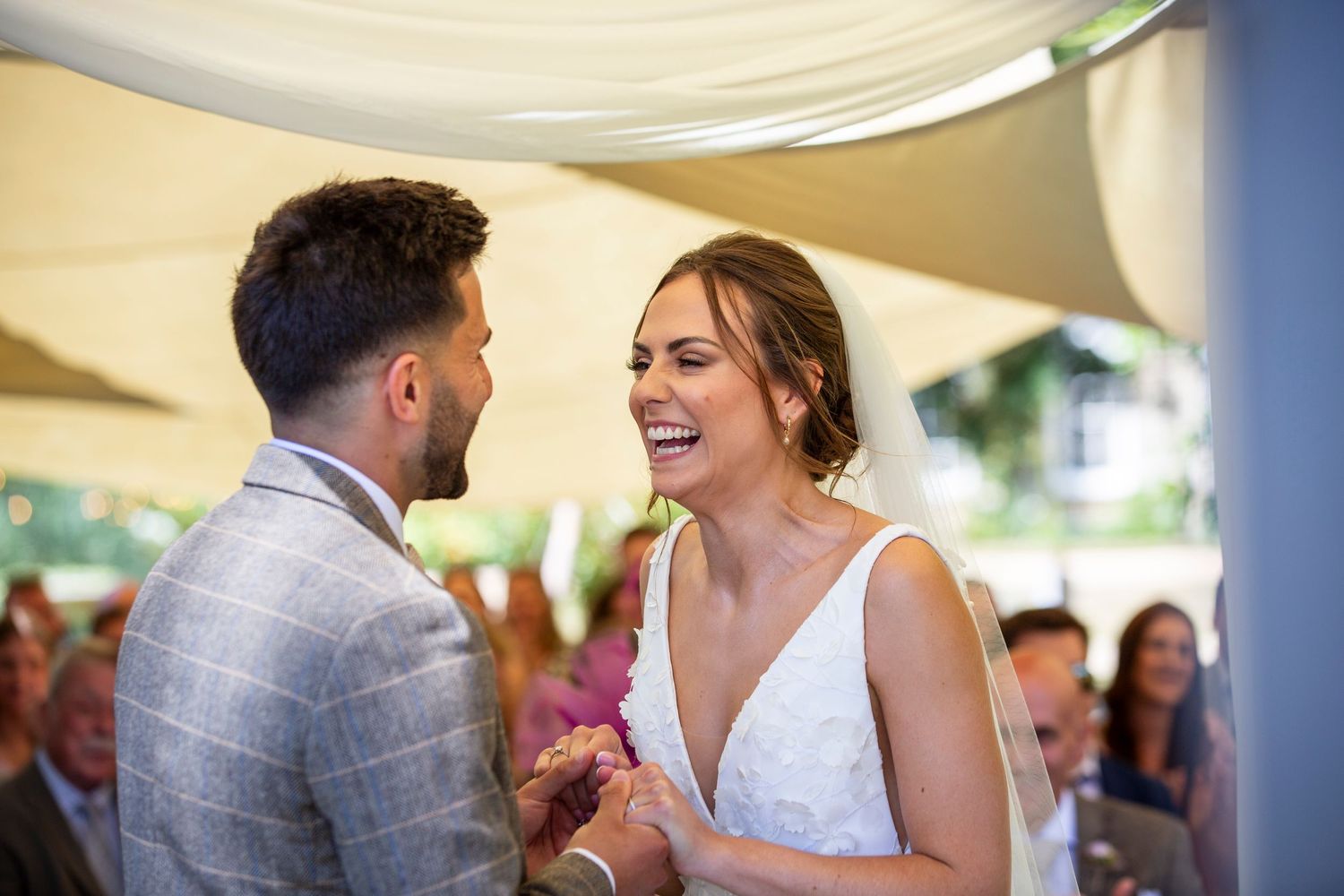Wedding party celebrating under a white tent canopy during an outdoor reception.