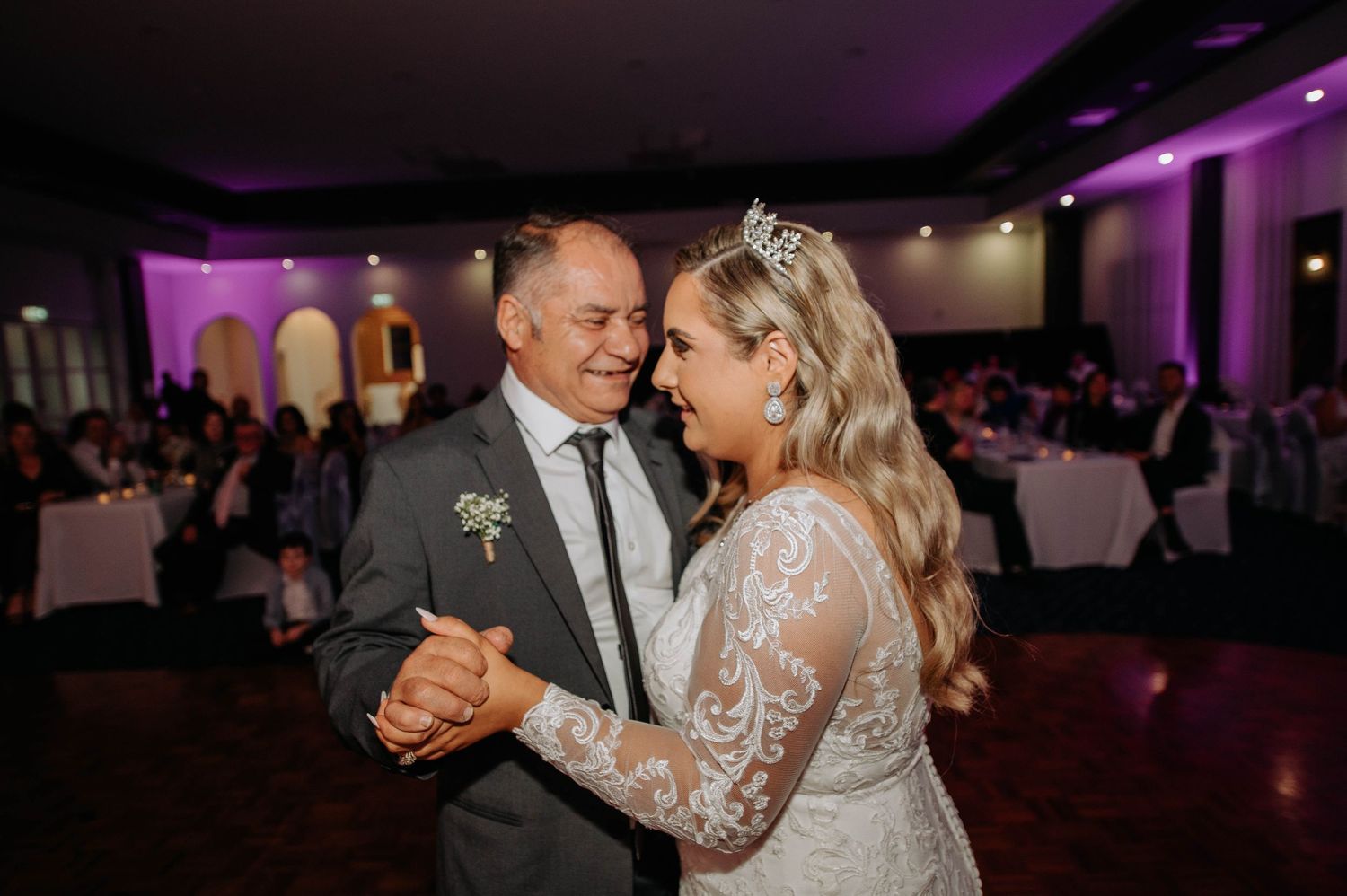 Couple shares intimate first dance at wedding reception under purple ambient lighting.