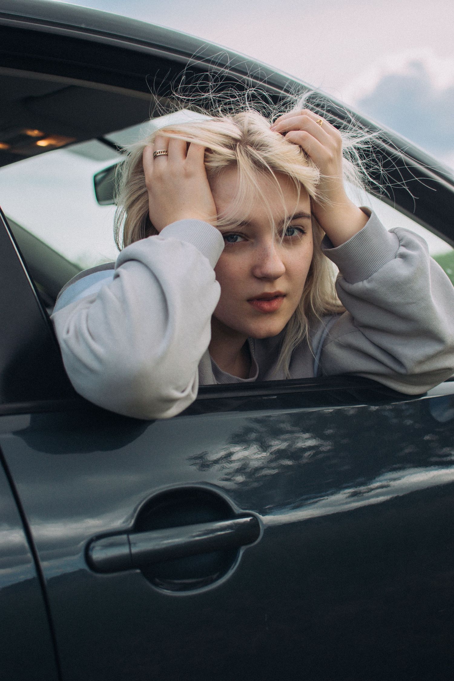 Person with blonde hair fixing their hair while sitting in car.