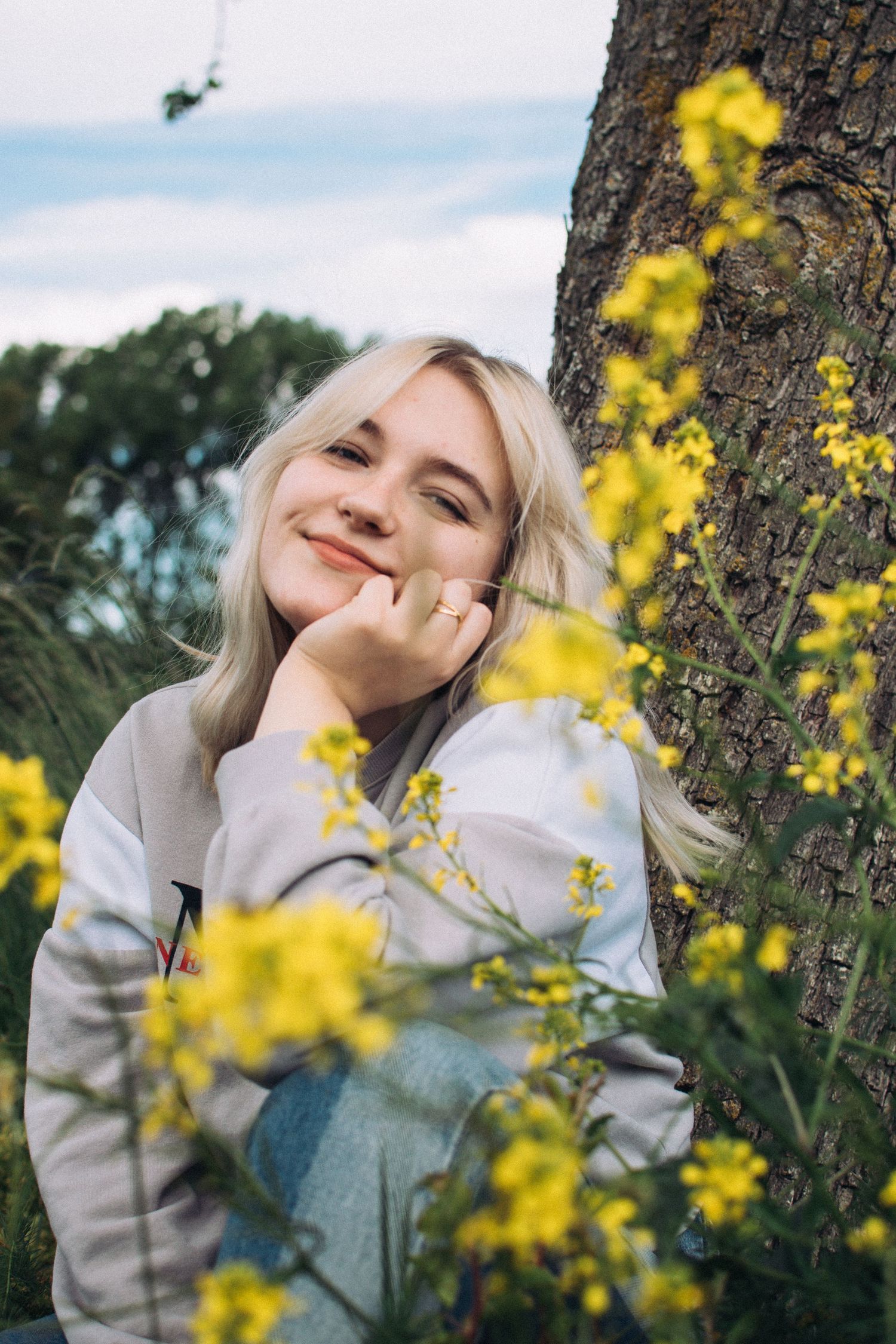 Person posing by tree with yellow flowers in natural outdoor setting.