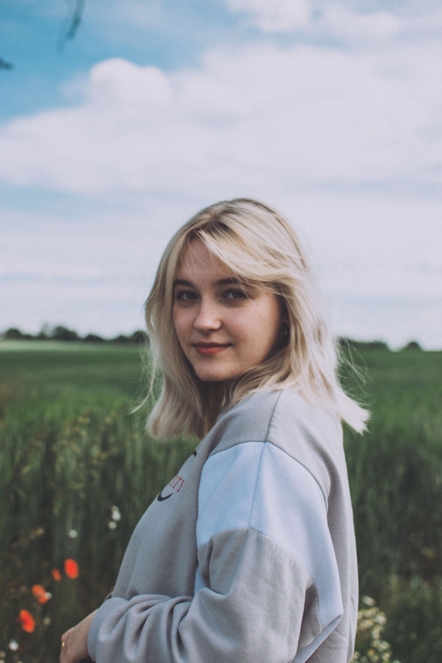 Person wearing gray sweatshirt standing in field under cloudy sky.