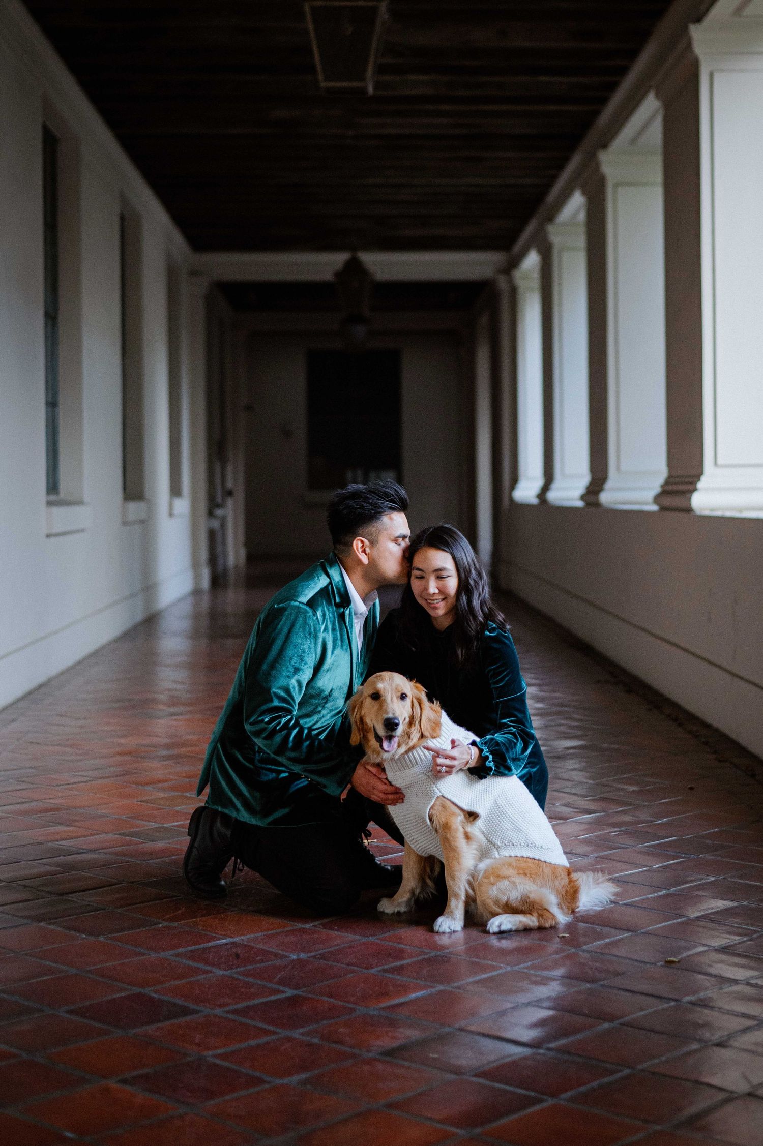 Couple sitting with their dog in a dimly lit hallway with terracotta floors.