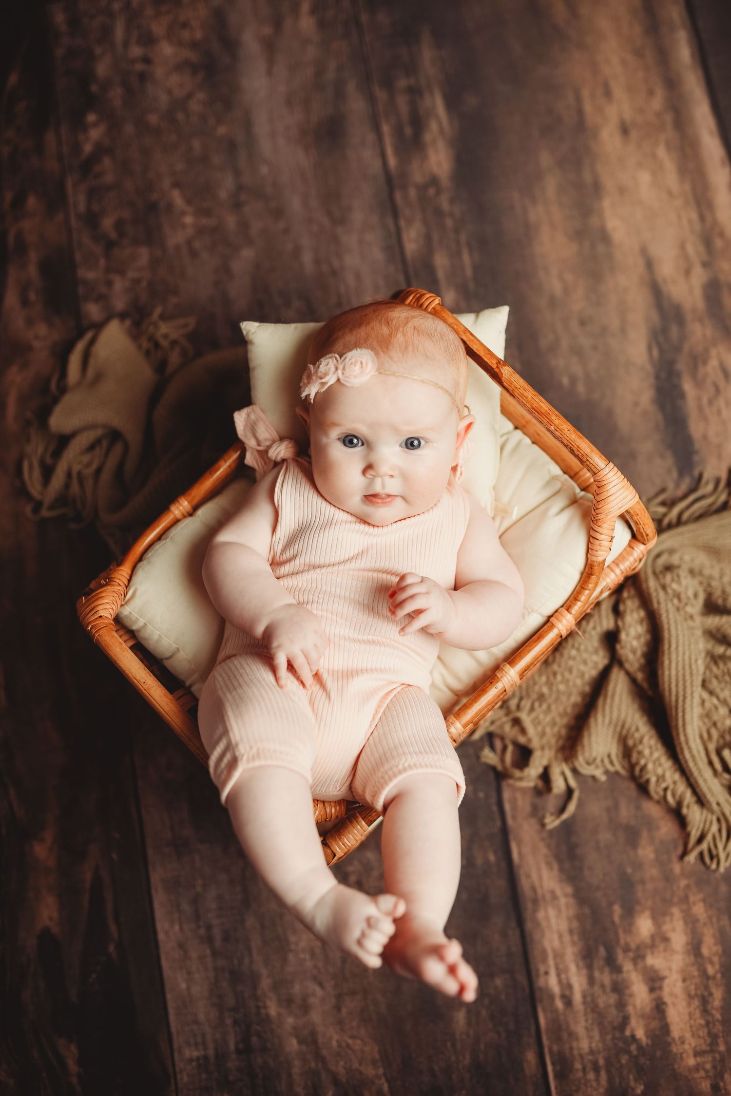 Baby in pink outfit resting in woven basket against dark wood backdrop.