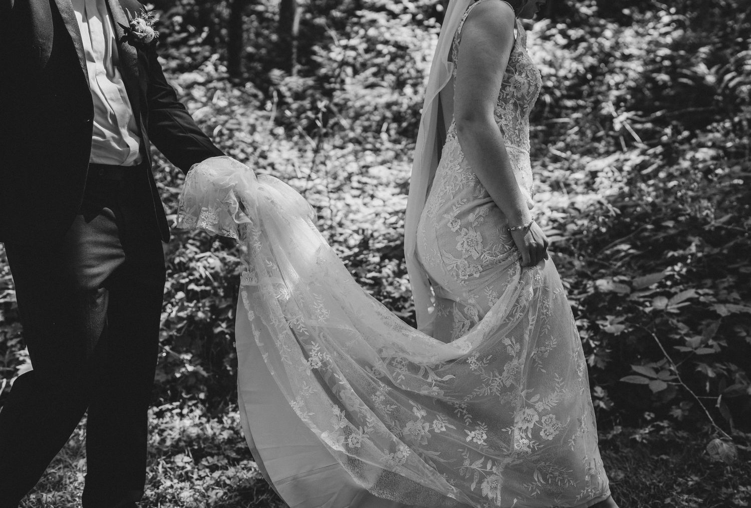 A black and white photo showing the intricate lace detail of a flowing wedding dress train.