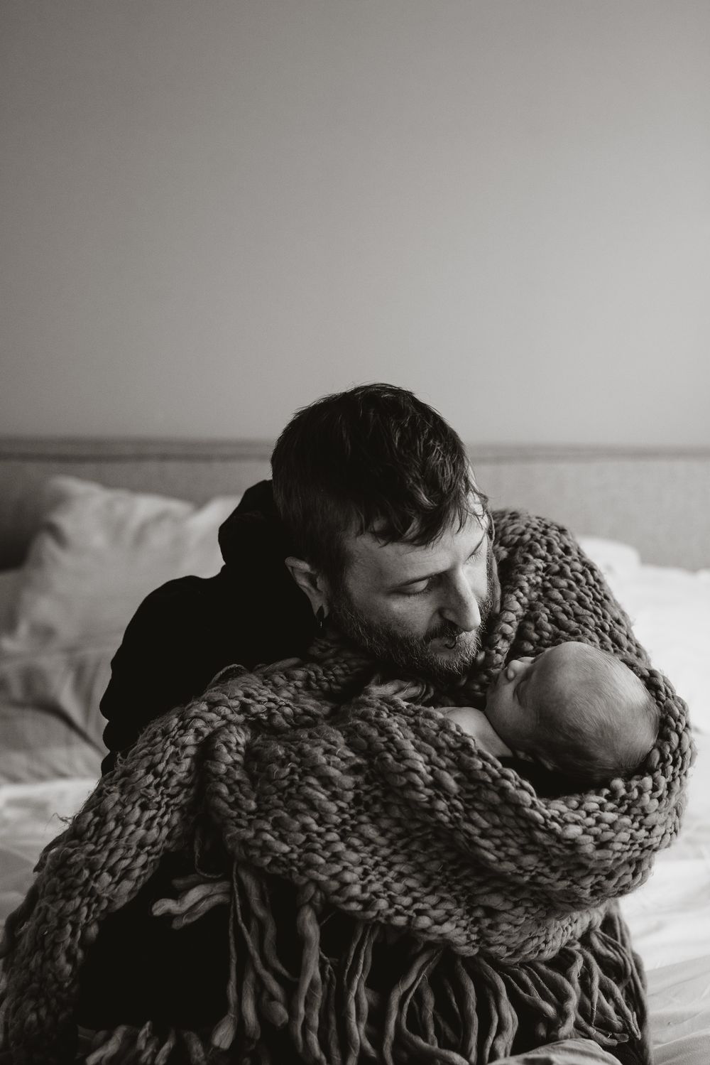 Intimate black and white image of person in chunky knit sweater on bed.