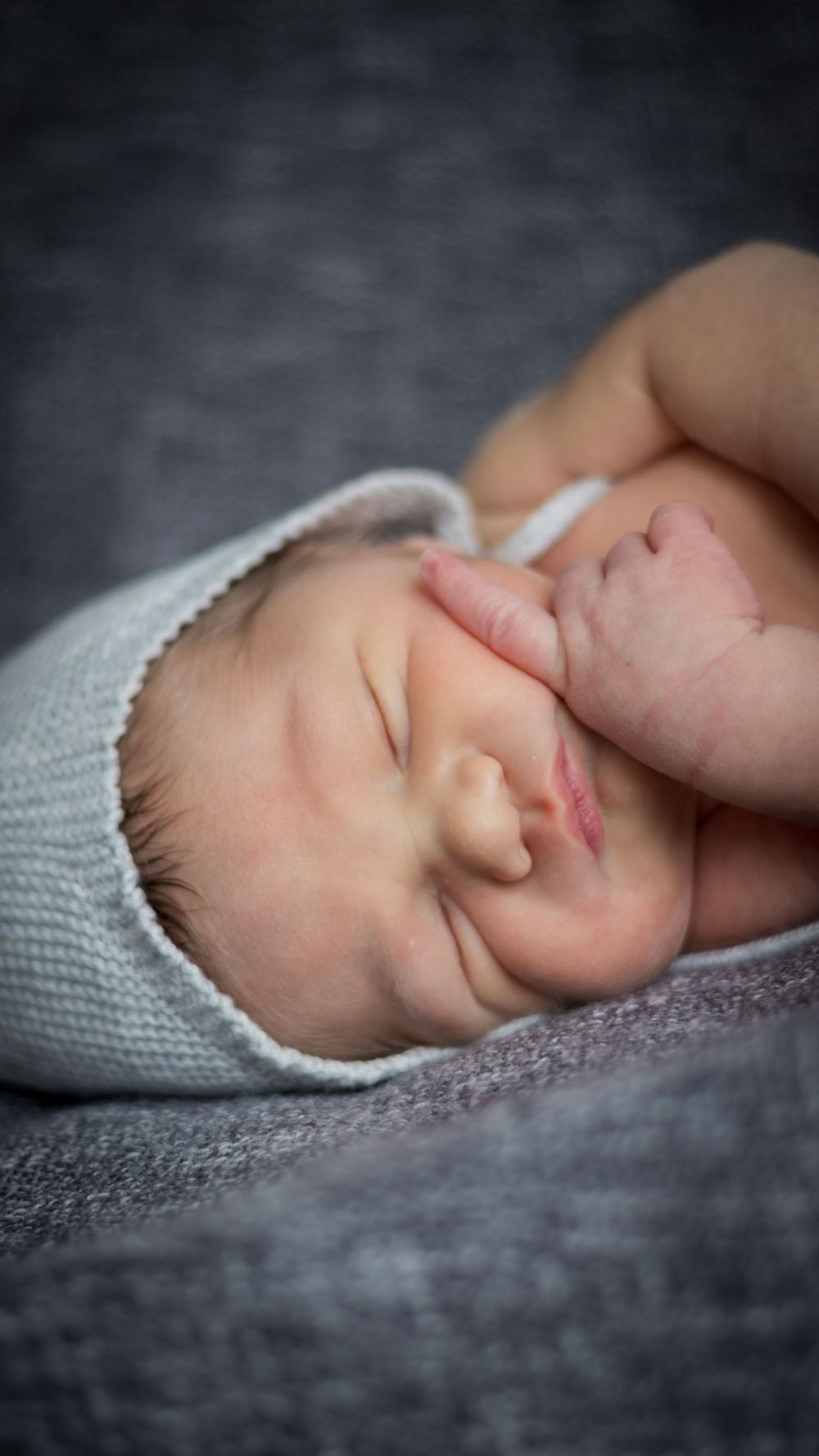 Peaceful closeup of newborn baby in soft grey knit hat.