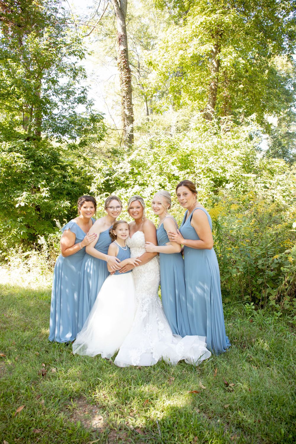 Wedding party in light blue dresses poses together in a sunny garden setting.